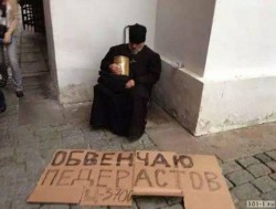 Человек в черной одежде сидит на улице с табличкой