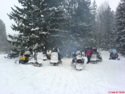 Группа людей рядом со снегоходами в лесу зимой