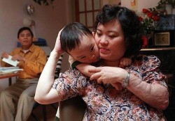 Женщина обнимает ребенка, сидя на стуле. Мужчина на заднем плане