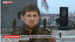 Мужчина на фоне памятника и флагов, говорит в камеру