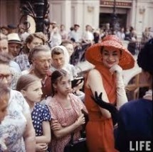 Женщина в красном платье и шляпе среди зрителей