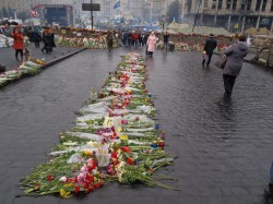 Цветы и свечи на площади, люди проходят мимо