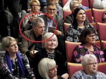 Мужчина в очках сидит среди зрителей на мероприятии