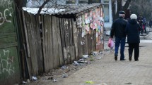 Пара людей идет по грязной улице рядом с забором