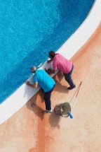 Два человека работают у края бассейна, укладывая плитку