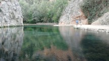 Два человека стоят у берега прозрачного водоема среди скал