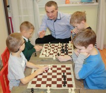 Четыре ребенка играют в шахматы с преподавателем