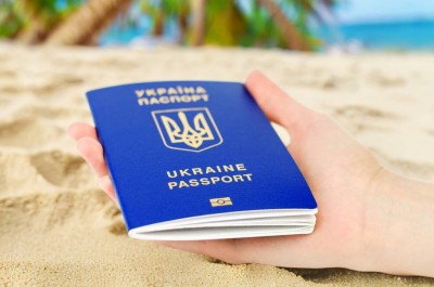 Рука держит украинский паспорт на пляже в Испании