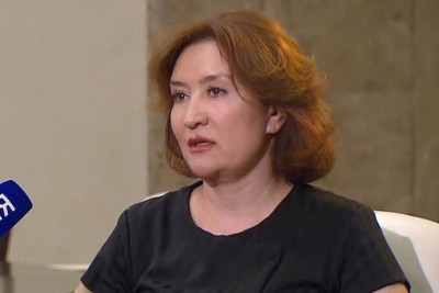 Женщина с короткими рыжими волосами в черной одежде.