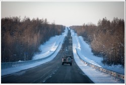Заснеженная дорога с автомобилем на фоне леса