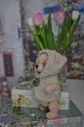 Мягкая игрушка медведя в сером капюшоне на фоне цветов
